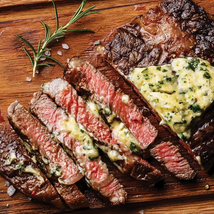 Sliced steak with herb butter on a wooden cutting board