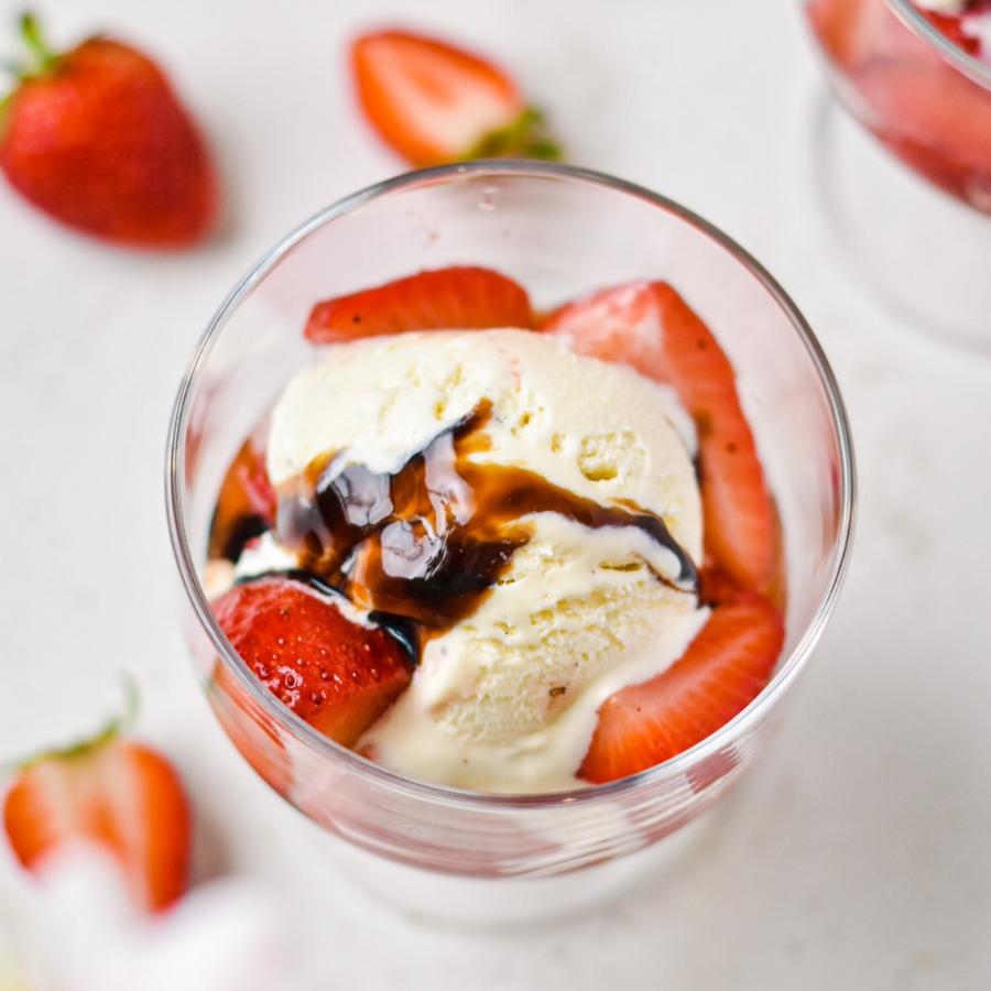 Glass bowl with ice cream, strawberries, and a drizzle of syrup on a light background