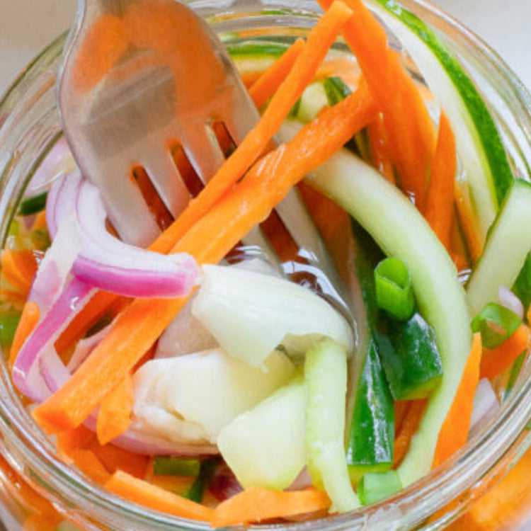 Glass jar filled with pickled vegetables including carrots, cucumbers, and onions, with a fork inside.