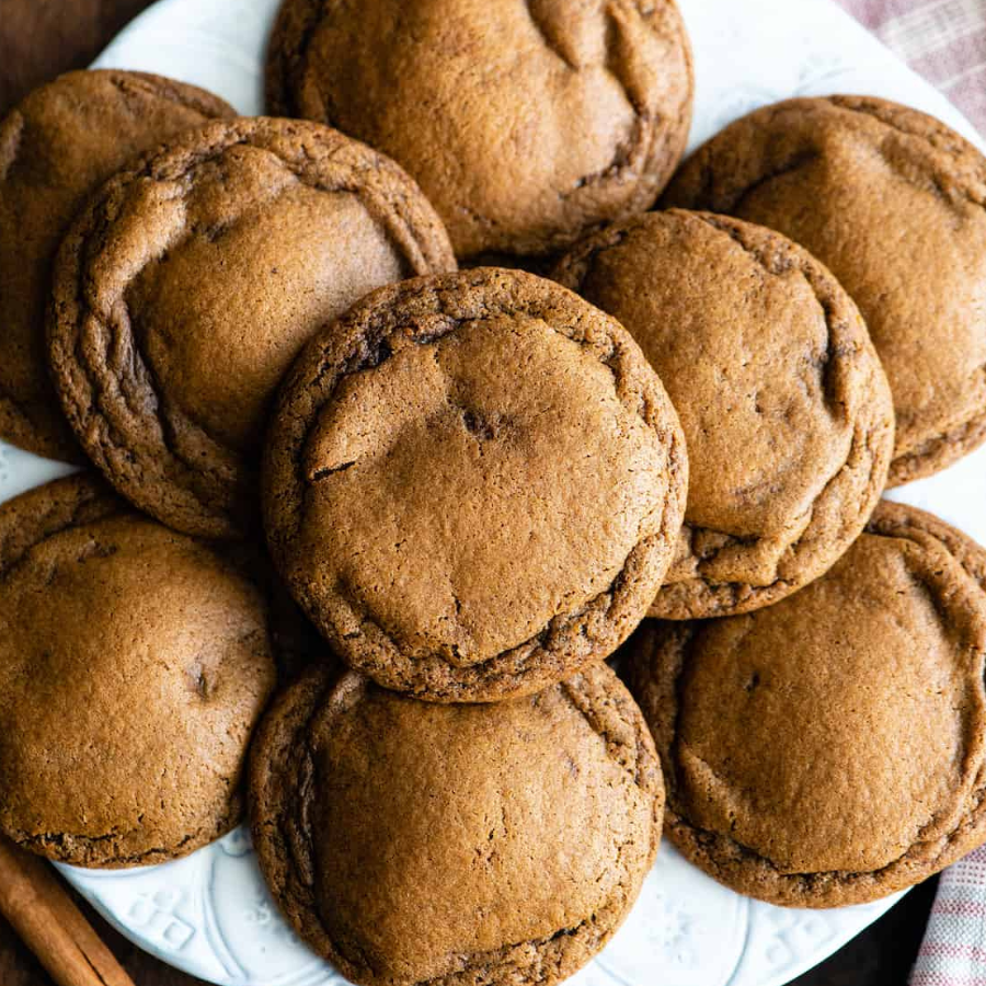 A pile of golden-brown chocolate chip cookies on a white plate, photographed from above.