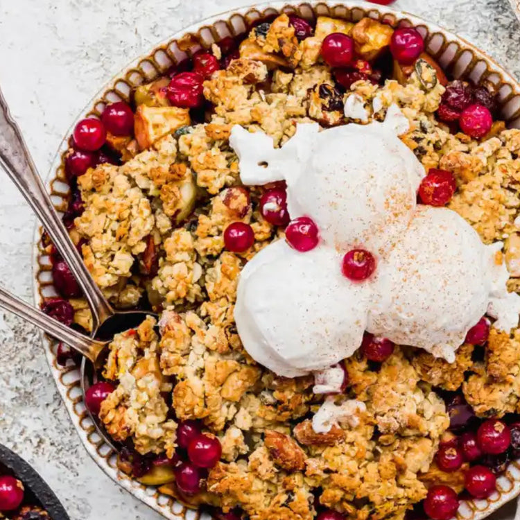 Peach cobbler with cranberries and vanilla ice cream in a bowl on a textured surface