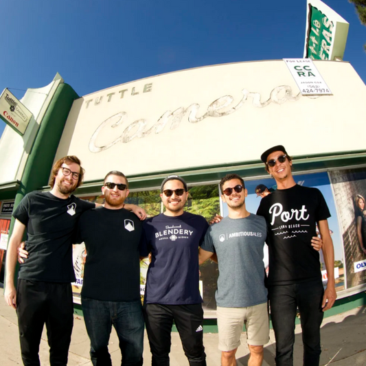 Five men standing together in front of a storefront with large 'Tuttle Camera' signage under a blue sky.