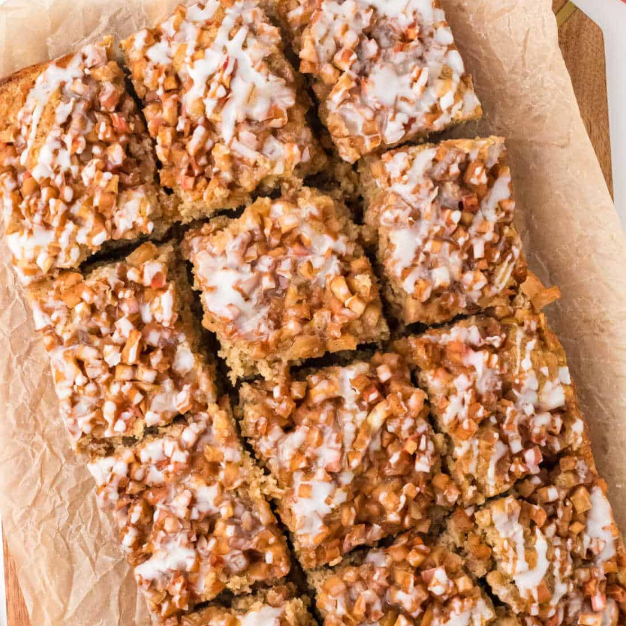 Overhead close-up of cut square slices of a dense baked loaf topped with white icing and chopped nuts, arranged on parchment paper.