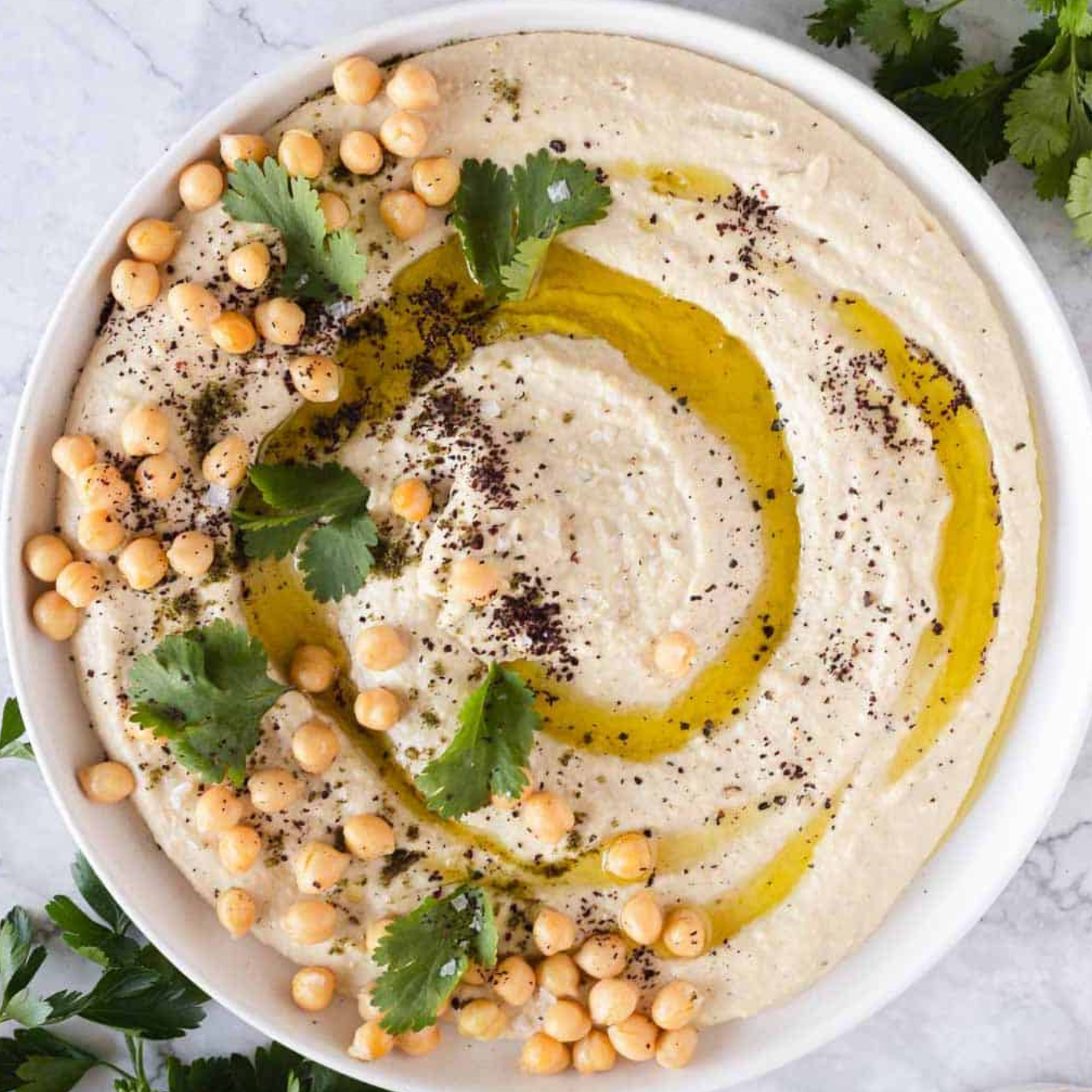 Hummus bowl with chickpeas, olive oil, and herbs on a marble surface