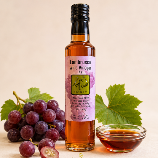 Bottle of Lambrusco Wine Vinegar with grapes and a small bowl of vinegar on a beige background