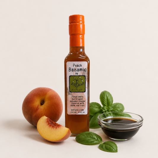 Bottle of Peach Balsamic with peaches, basil leaves, and a small bowl of liquid on a light background