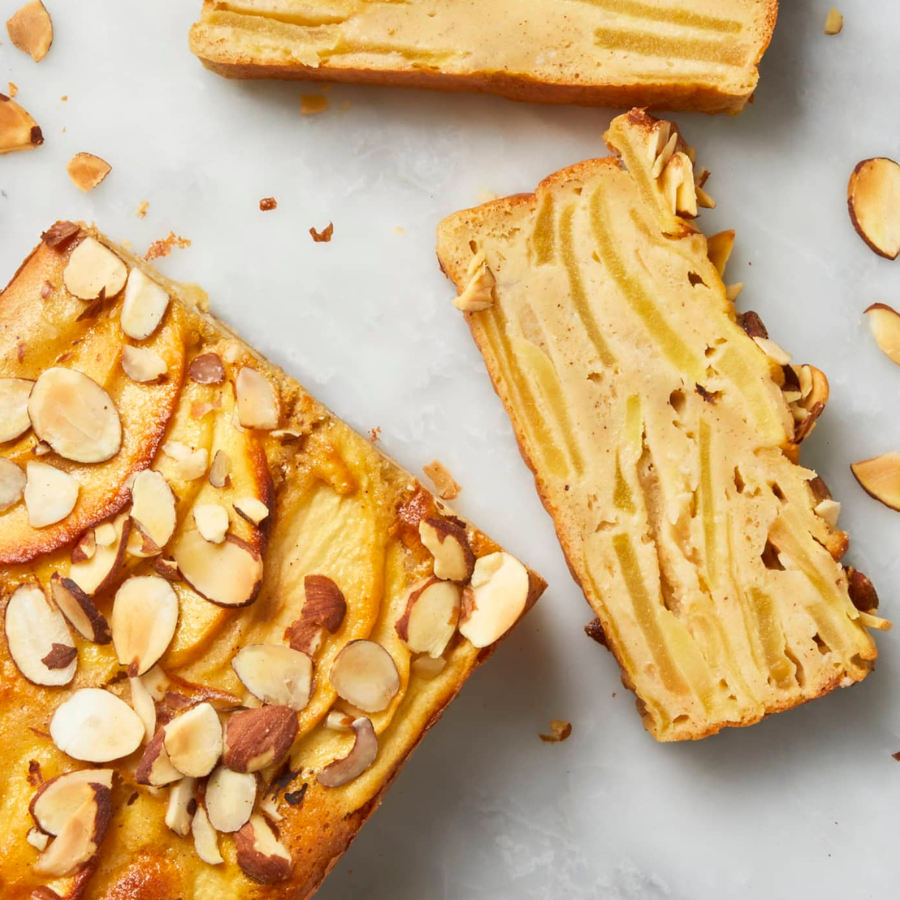 Slices of almond cake with sliced apples and almonds, arranged on a light marble surface.