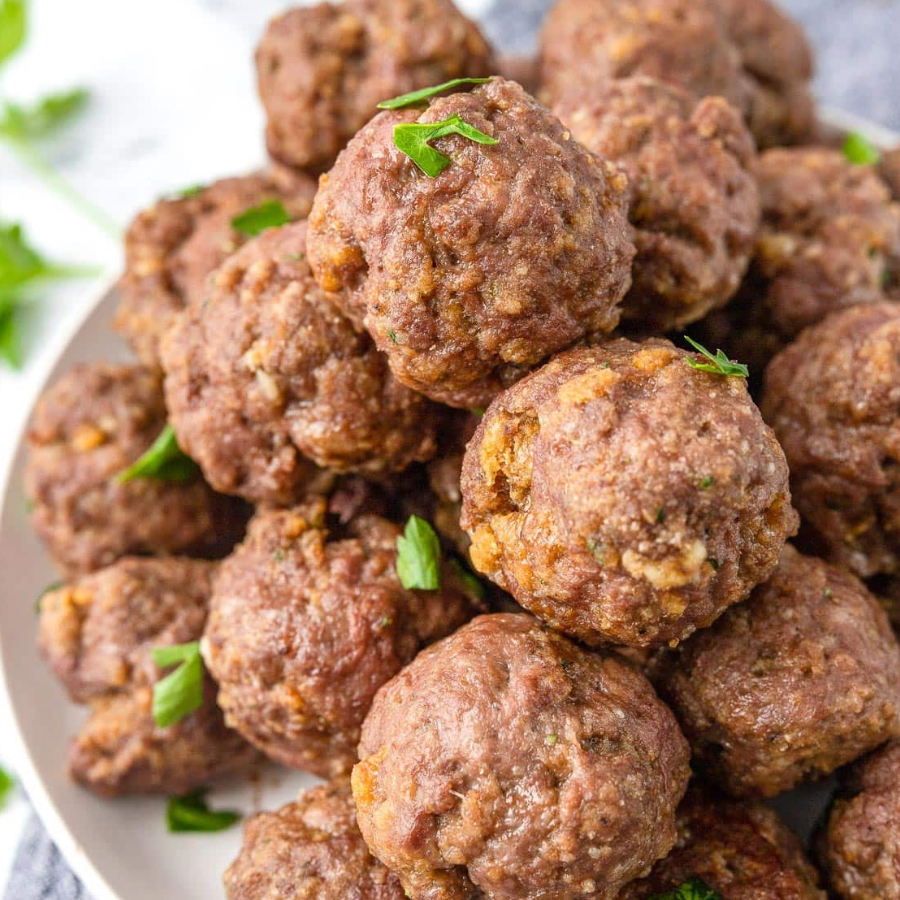 A close-up shot of a pile of cooked meatballs garnished with chopped green herbs on a white plate.