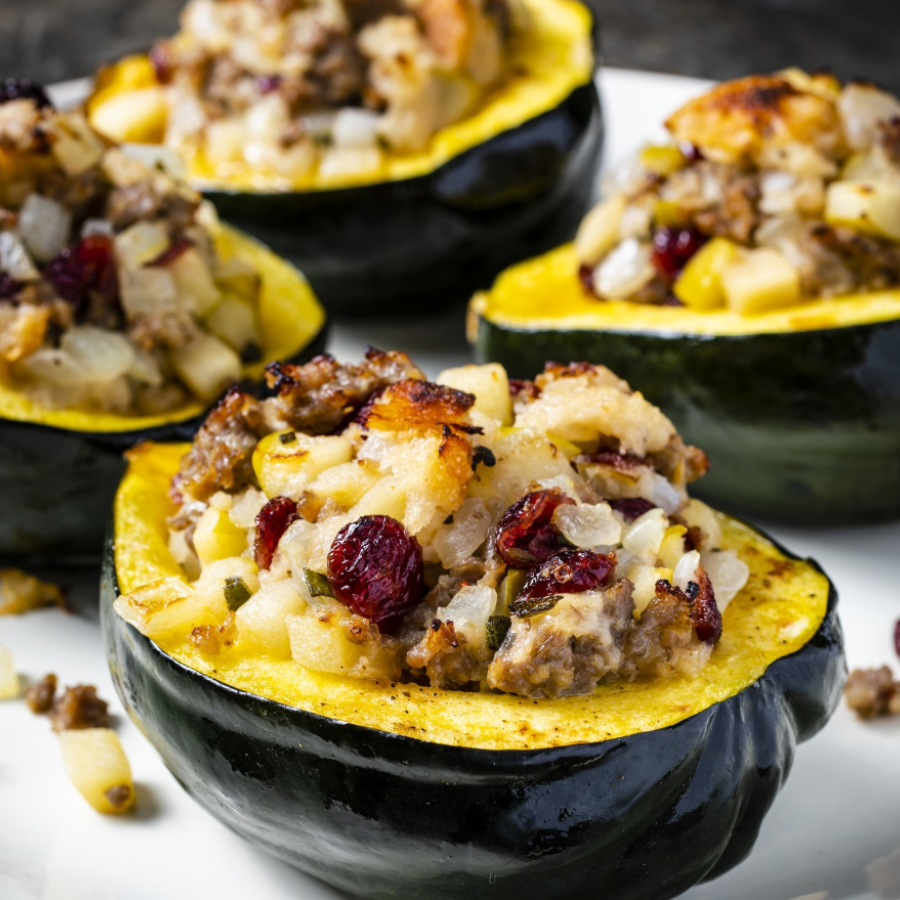 Four halves of acorn squash stuffed with a savory mixture of ground meat, diced potatoes, onions, and dried cranberries, arranged on a white plate.
