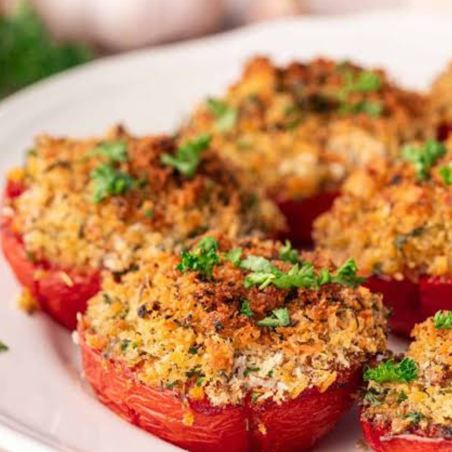 Stuffed red bell peppers topped with a golden-brown breadcrumb and herb mixture, garnished with fresh green parsley, served on a white plate.