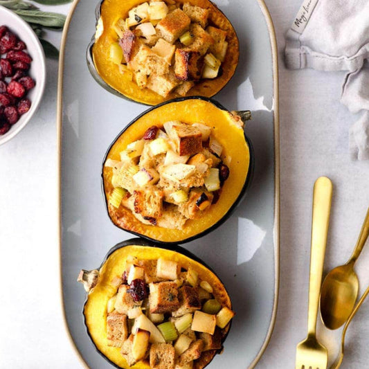 Three acorn squash halves filled with stuffing on a gray plate with gold utensils.