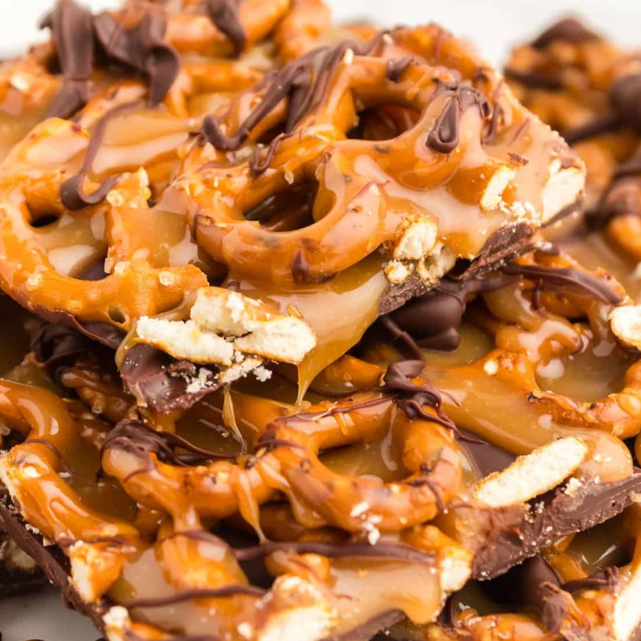 Close-up of caramel-topped pretzel pieces with drizzles of caramel and chocolate, mixed with crumbled peanuts and white chocolate pieces.