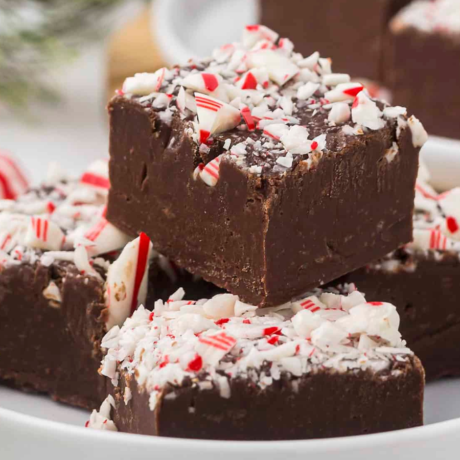 Chocolate peppermint fudge bars topped with crushed candy canes, stacked on a white plate.