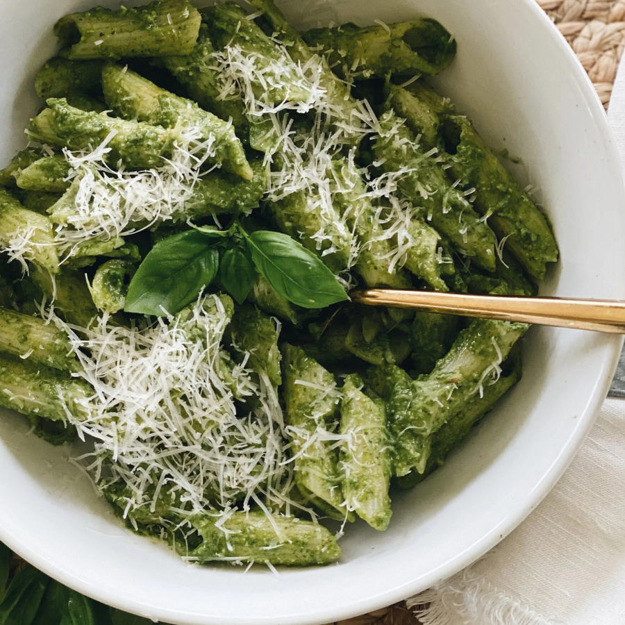 Green pasta dish with basil and parmesan in a white bowl
