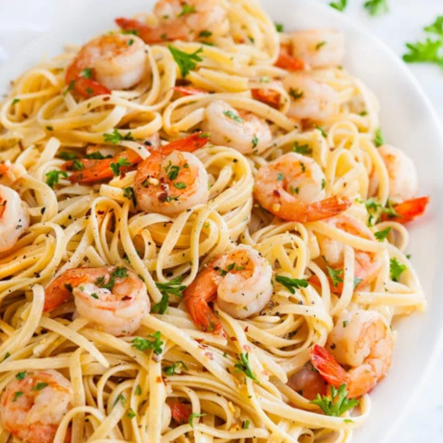 A close-up shot of a pasta dish featuring shrimp and herbs on a white plate.