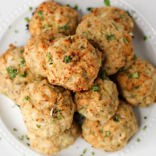 A pile of golden-brown baked meatballs garnished with chopped green herbs on a white plate.
